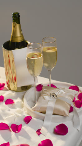 Vertical-Video-Of-Table-Set-To-Celebrate-Marriage-With-Champagne-And-Rings-On-Satin-Cushion